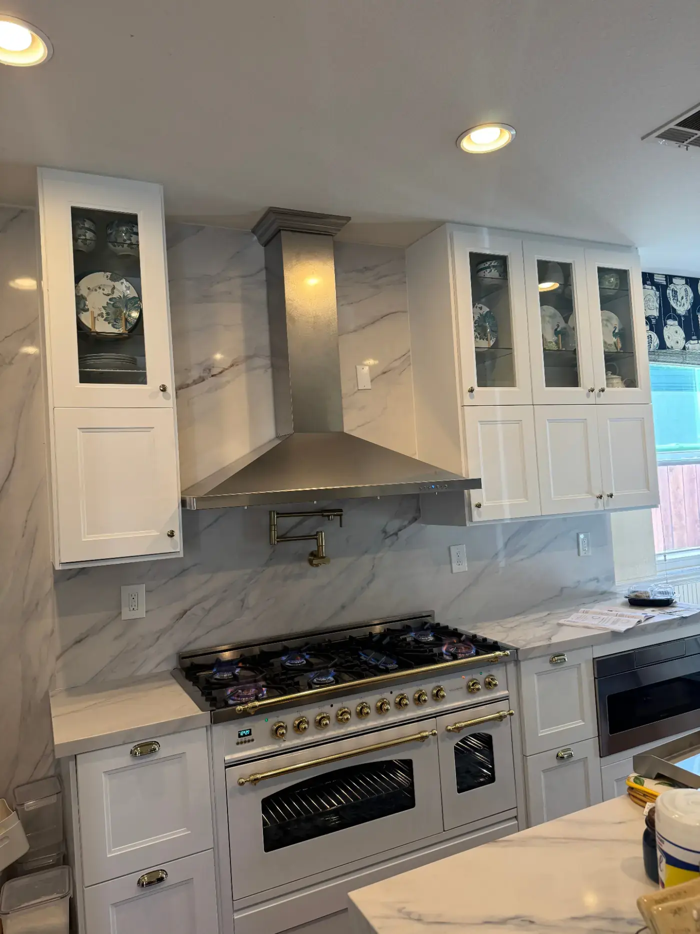 Custom kitchen with marble slab backsplash, brass pot filler, professional dual-oven gas range, and glass-front display cabinets
