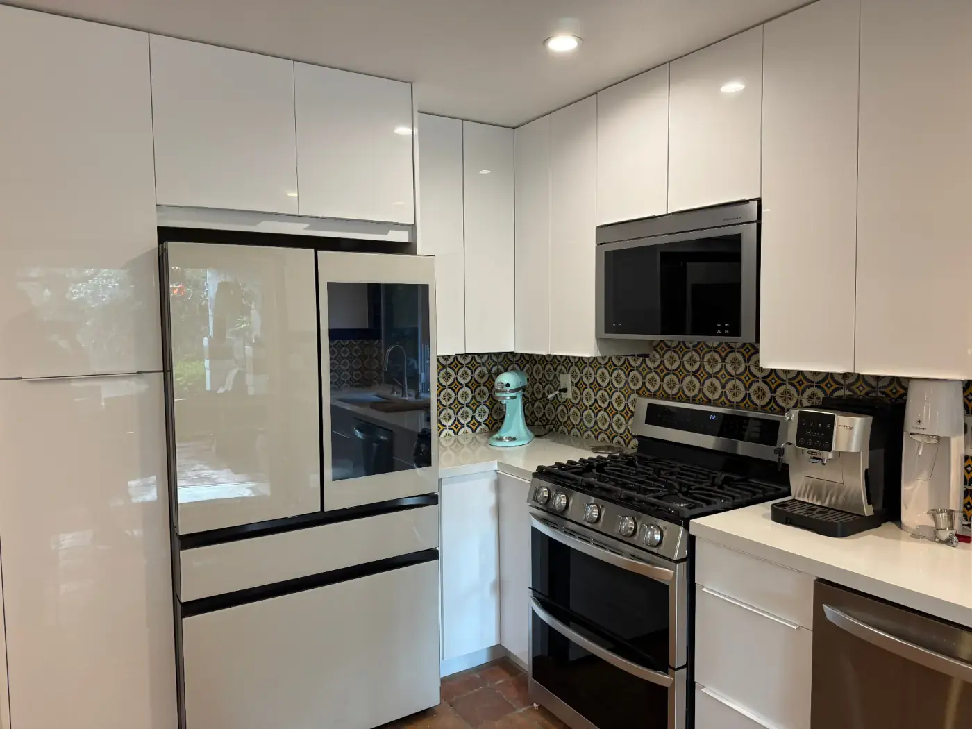 Sleek high-gloss white kitchen with black-trim refrigerator, patterned blue and yellow tile backsplash, and stainless steel double oven