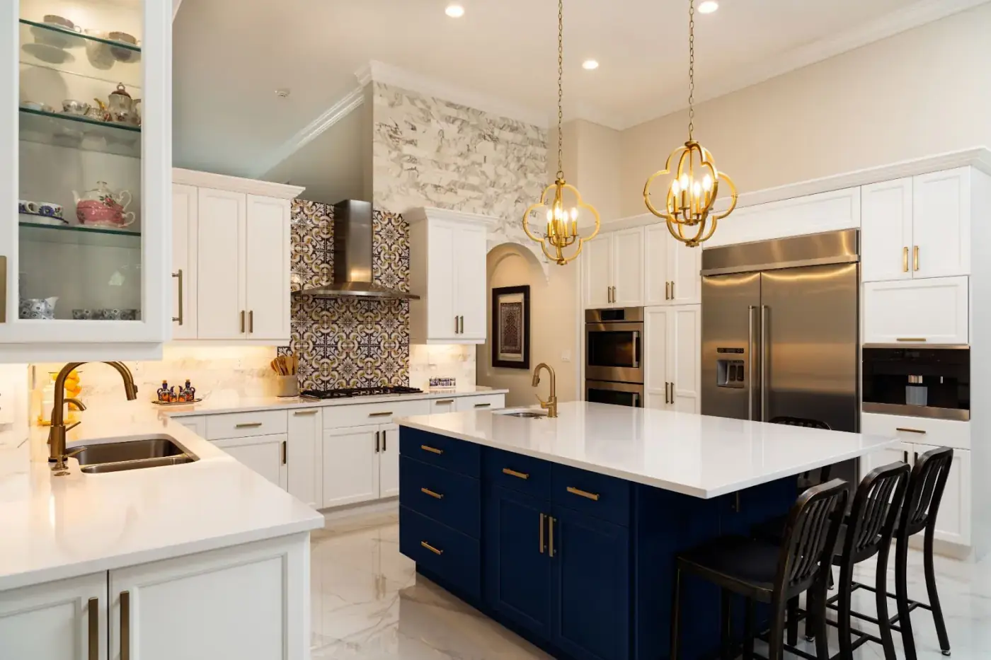 Grand transitional kitchen with navy blue island, white cabinetry, brass quatrefoil pendants, and decorative Spanish tile backsplash