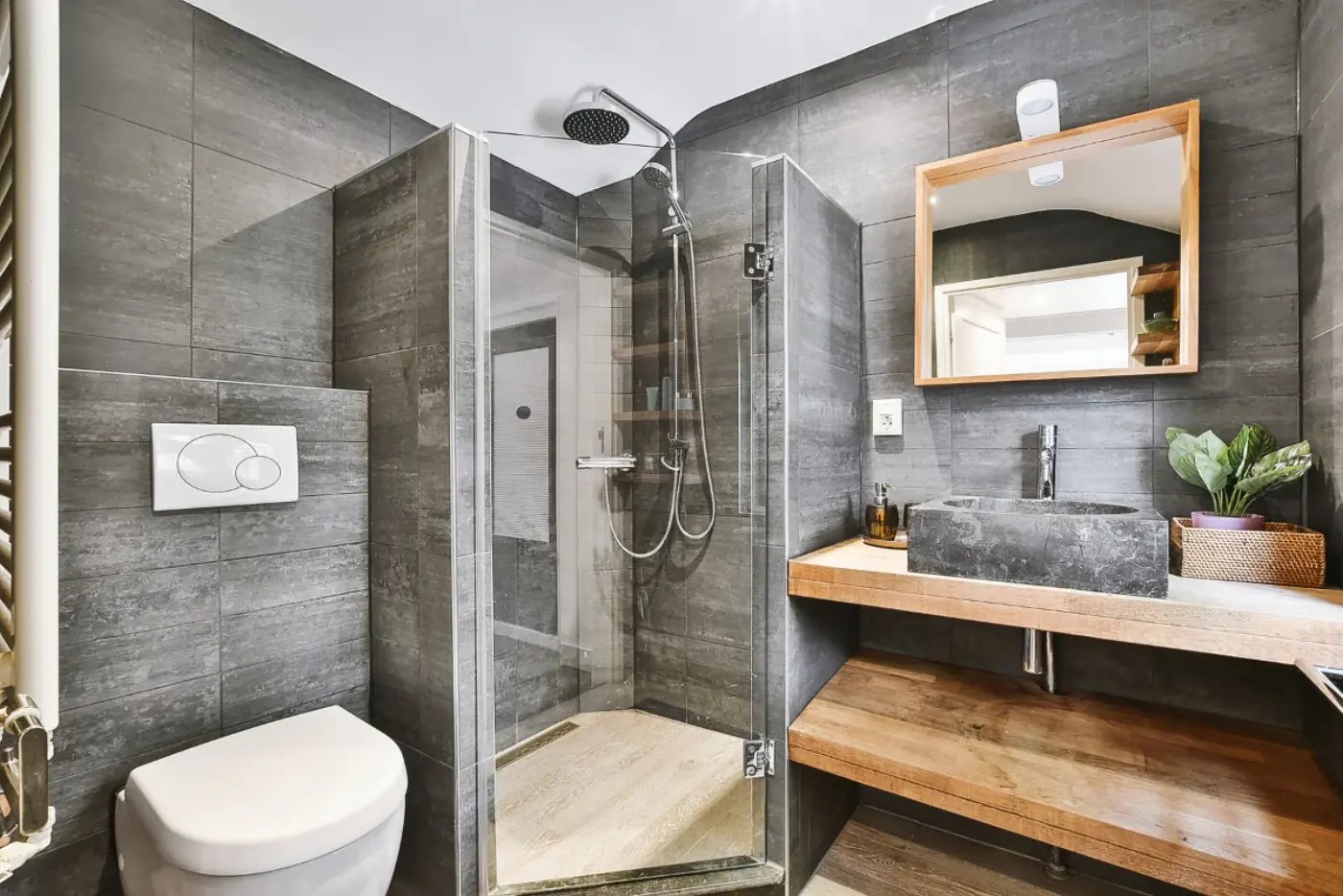 Contemporary bathroom with gray stone tile walls, glass walk-in shower, and a stone vessel sink on a wood vanity