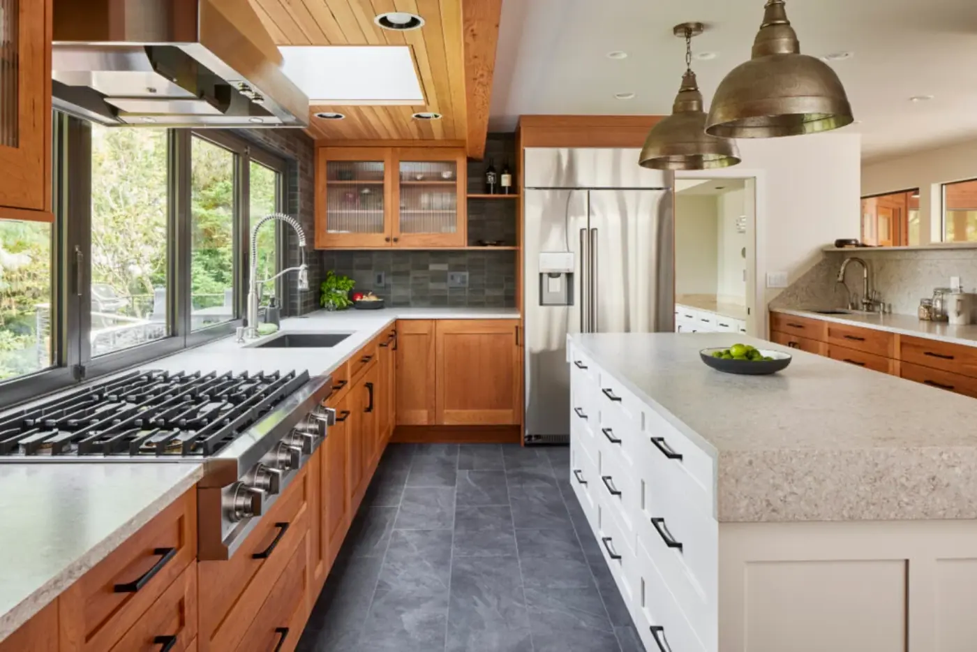 Transitional kitchen with cherry wood cabinets, white island, slate tile floor, and industrial pendant lights