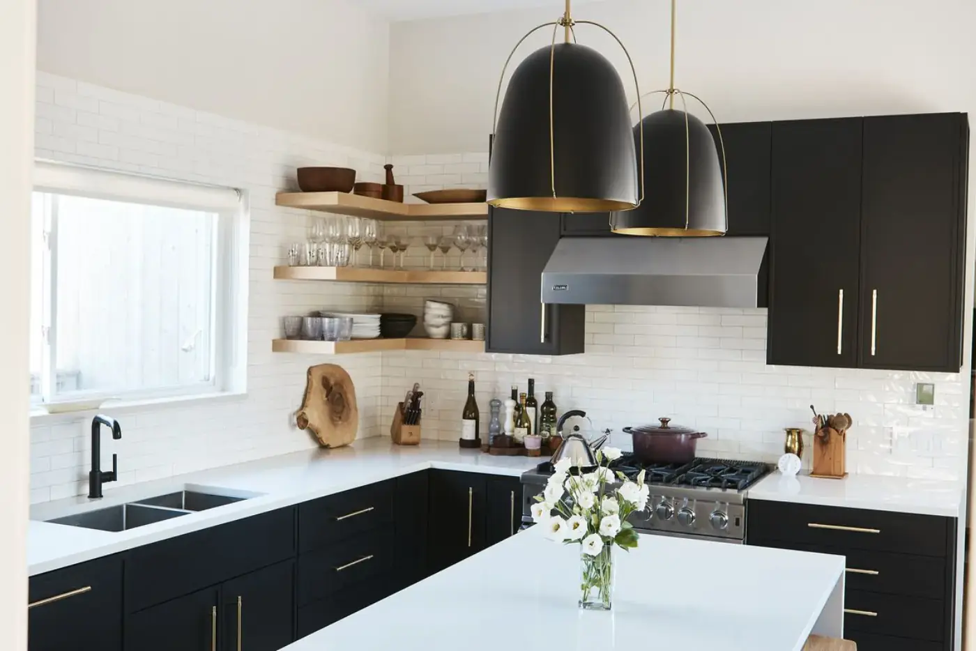 Modern black and white kitchen with subway tile backsplash, brass hardware, oversized pendants, and floating wood shelves