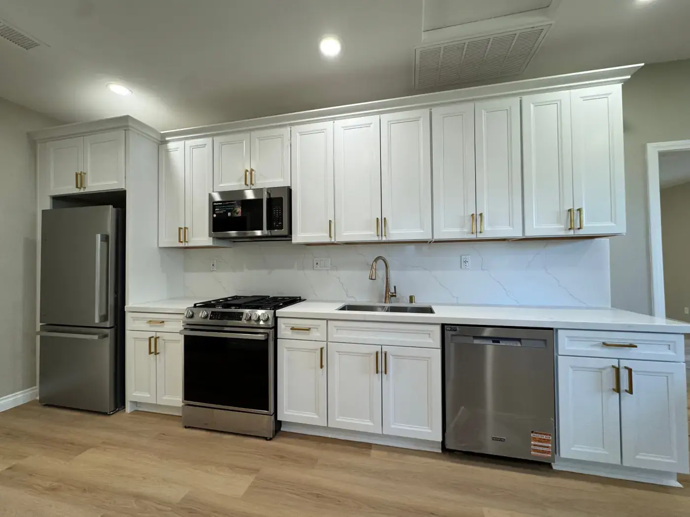 Newly remodeled white shaker kitchen with brass pulls, quartz waterfall backsplash, stainless appliances, and light wood floors